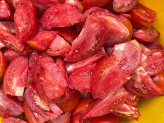 Red ripe tomatoes are coarsely sliced in a plate.
