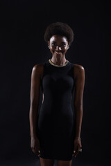 Naklejka premium Standing smiling portrait of african american woman with afro hairstyle on black studio background.