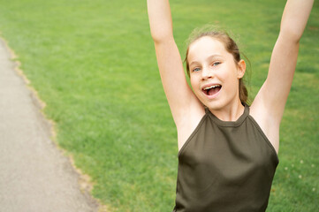 Happy teenage girl with hands up, against green summer park. Confident young woman portrait Copy space