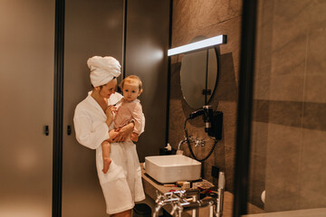 Lady during morning make-up picked up her daughter and tickles her with makeup brush. Portrait of...