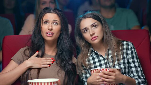 Closeup two female friends watching film at cinema gossiping discussing actors melodrama scene