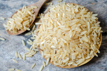 Top view of dry organic brown rice seed pile in wooden bowl and spoon on grunge background