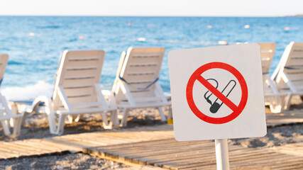 No smoking sign on the beach in summer. There are sun loungers on the background.