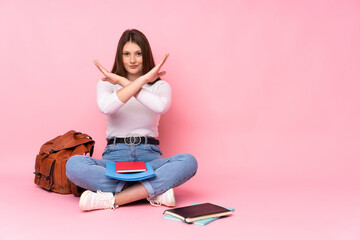 Teenager caucasian student girl sitting on the floor isolated on pink background making NO gesture