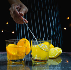 man stir ice and lemon juice in glass beside orange juice glass on table, bartender prepare fruit...