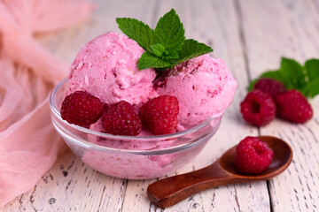 Raspberry ice cream in a glass bowl on a white wooden background.
Close-up.