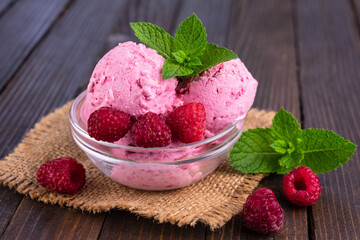 Raspberry ice cream in a glass bowl on a wooden background