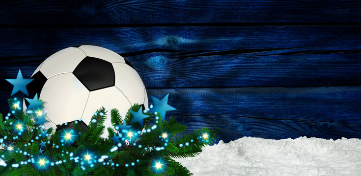 Soccer christmas bauble in snow with christmas decoration and fir branch. Blue wooden background. Christmas greeting