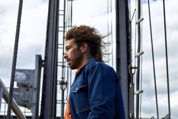 portrait d'un bel homme trentenaire caucasien sexy avec une barbe et des cheveux longs habillés mode  années 80 en extérieur sur une écluse  © mariesacha