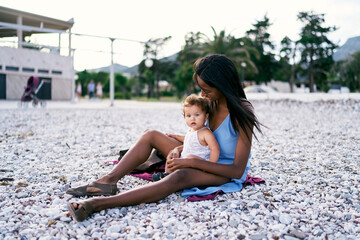 Fototapeta na wymiar Mom hugs little girl sitting on the beach