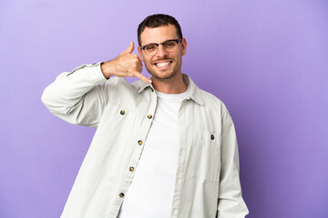 Brazilian man over isolated purple background making phone gesture. Call me back sign