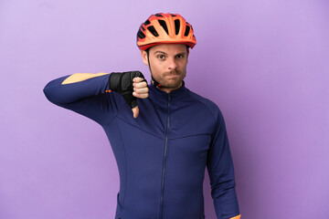 Young Brazilian cyclist man isolated on purple background showing thumb down with negative expression