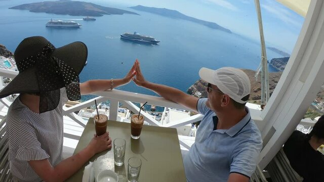 Romantic couple woman and men relaxing having a coffee drink sitting on the balcony with nice view of caldera in Santorini, Greece