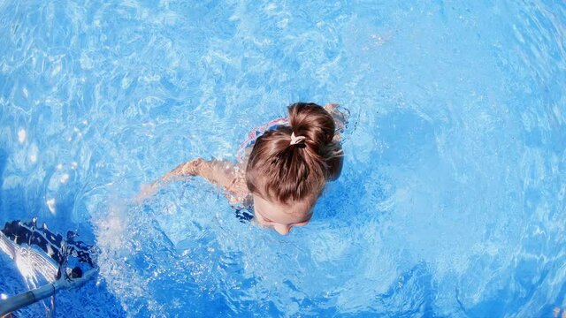 Top view of lhappy ittle smiling girl swimming in pool with flippers on legs, slow motion