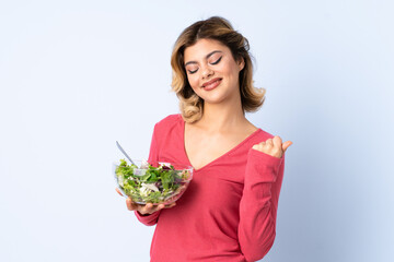 Teenager woman with salad isolated on blue background celebrating a victory