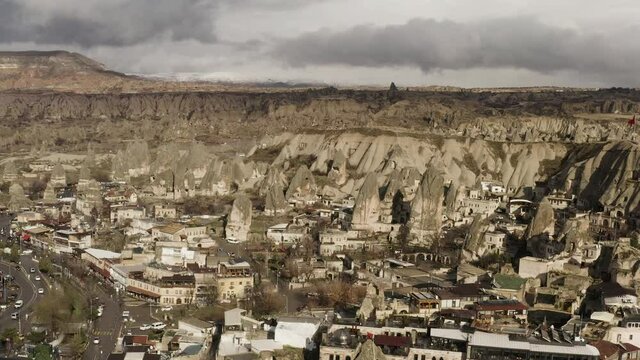 Aerial view of a small town located by the mountain range. Action. Red turkish flag waving on a rock top, sunny village in dry area.