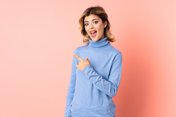 Young Russian woman isolated on pink background surprised and pointing side