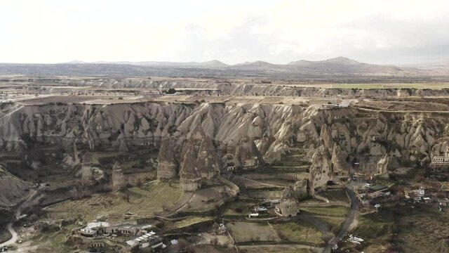 Aerial view from drone of mountains and rocks in Cappadocia near Goreme, Turkey. Action. Beautiful rocky valley with houses on cloudy sky background.