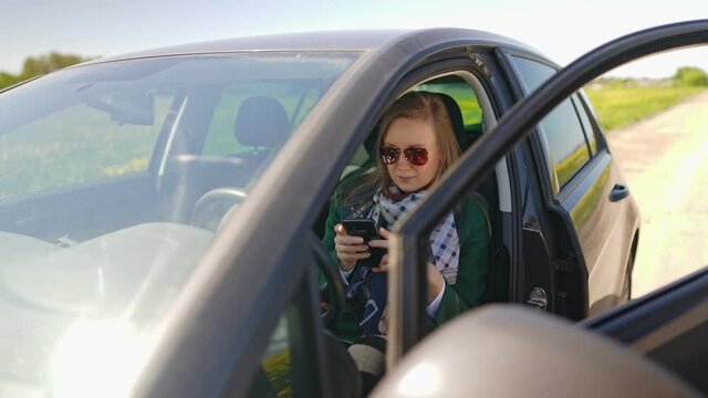 Woman sitting in car and using mobile phone.