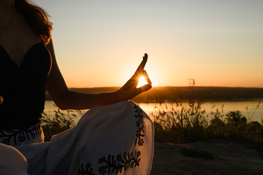 Female sit in litus pose at sunset, woman meditate in yoga lotus pose outdoors with raising sun at horizon