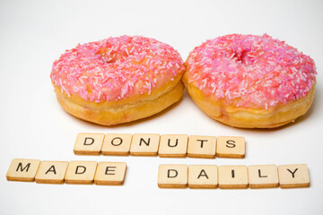 Two Iced Ring Donuts On A White Background With A Sign Reading Donuts Made Daily