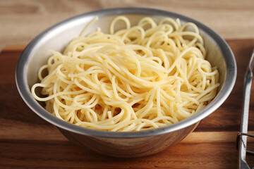 Cooked spaghetti in metal bowl on cuttingboard