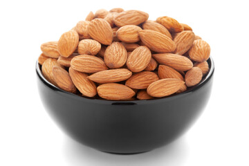 Close-up of brown almonds (Prunus dulcis) kernels in a black ceramic bowl over white background.