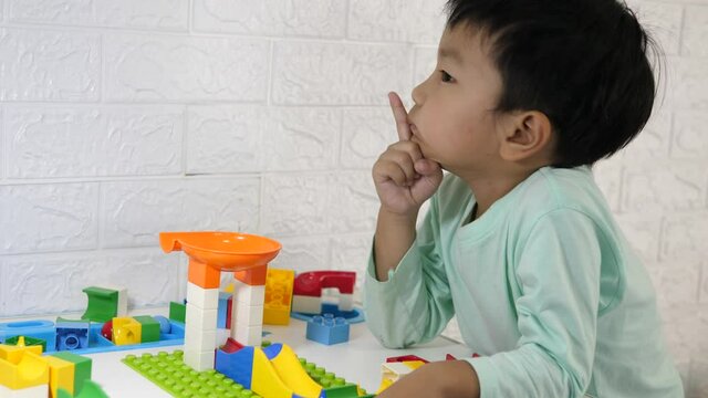 Asian child boy thinking idea while playing block at home. Kid learning to build toy. Concept of childhood, learning, thinking, creativity, education.