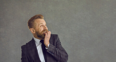 Profile view funny scared bearded young man in suit jacket biting nails and looking to the side at...