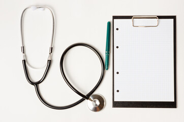 In the doctor's office, on the table is a stethoscope, a medical device for listening to the heartbeat, a tablet with a sheet of paper for recording, copy space