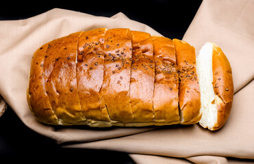 Sliced soft wheat bread close up view above a brown cloth on isolated dark background