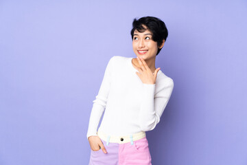 Young Vietnamese woman with short hair over isolated purple background looking up while smiling