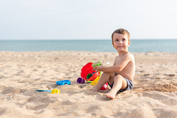 Adorable kid plays on the seashore in the sand with toys. Summer holidays
