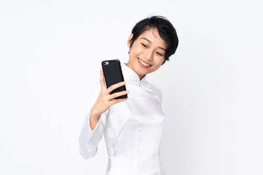 Young Vietnamese woman with short hair wearing a traditional dress over isolated white background making a selfie