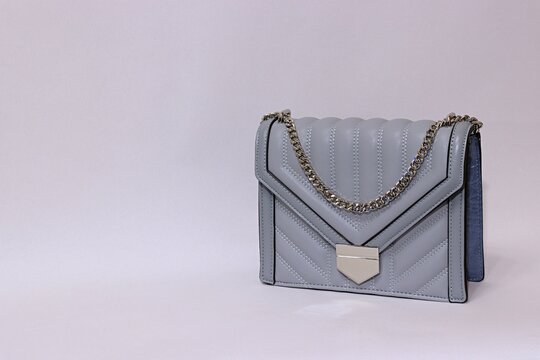 Gray women's handbag with a silver chain and silver clasp on a white and orange background.
