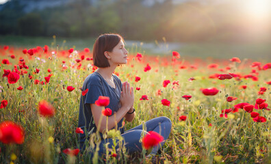 A beautiful woman meditates on a poppy field at sunset. Wellness well-being happiness concept.