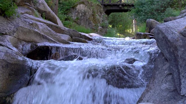 Fresh water waterfall in the foreground and wooden bridge in the background.