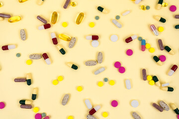Background from multi-colored pills and capsules. Beige background strewn with medicines. Top view