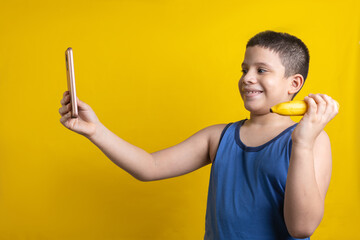 Latin child taking photo with mobile with a banana in hand, on yellow background