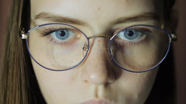 Close-up eyes of a teenage girl with glasses looks at the monitor, plays a game, reads, studies late at night
