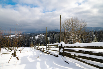 Evening in the mountains. Sunset, winter day. On the white snow the shadow of the fence. Wooden fence, the border between neighbors.
