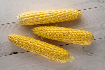 Three cobs of organic sweet corn on a wooden table, close-up, top view.