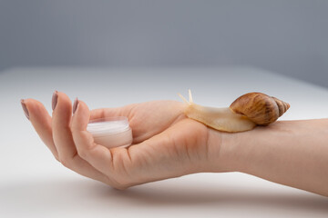 Close-up of a woman's hand with a small jar of moisturizer and a snail crawling on the skin. The use of snails in cosmetology.