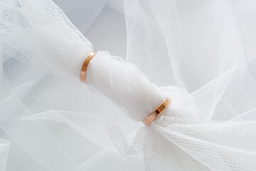 White mesh veil is threaded through the two golden wedding rings.