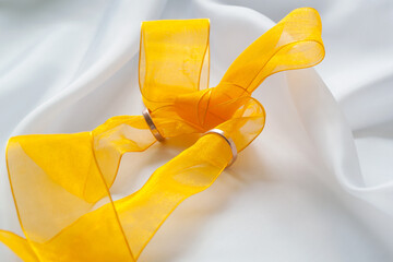 Gold wedding rings and bright yellow ribbon bow on white cloth.