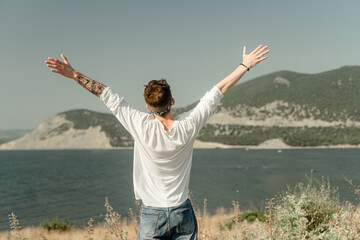 enjoys nature, view from the back, raised his hands up, shows a sign of peace, shows two fingers with his hands, relaxes against the backdrop of the mountains