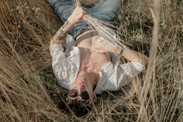 the guy lies on the grass in a shirt with an open torso, top view, in round sunglasses
