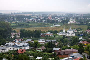 Obraz premium Panoramic top view of the historic old town of Suzdal with the roofs of houses and green foliage of trees on a cloudy summer day
