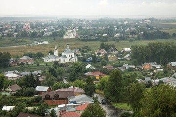 Fototapeta na wymiar SUZDAL, Vladimir Region, RUSSIA-August, 11,2021: panoramic view of the old town with the roofs of historical buildings and the green foliage of trees on a cloudy summer day