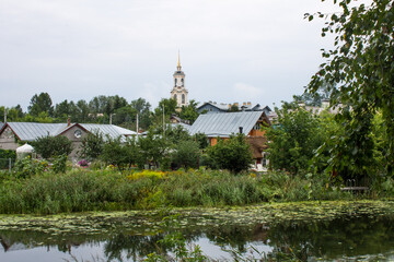 Fototapeta na wymiar Beautiful landscape-traditional Russian wooden houses on the bank of a small river and lush green foliage of trees in the old town of Suzdal Russia on a cloudy summer day